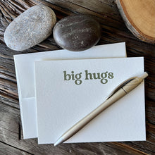 Load image into Gallery viewer, Single notecard with envelope - it says &quot;big hugs&quot; in olive green letterpressed ink, styled on a wooden table with river rocks, a gold pen and a sliced wood coaster.
