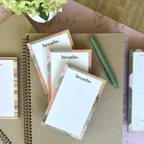 Three breathe notepads, styled with a green pen and other stationery items