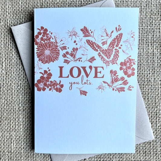 Greeting card with a white background and a dark pink illustration of flowers, bees and a buttefly with the text reading "LOVE you lots"