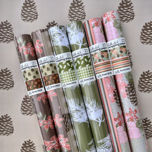 Load image into Gallery viewer, Rolls of packaged wrapping paper in plastic sleeves with sticker labels. Showing all 3 new patterns with pine, floral, stripe and gingham details
