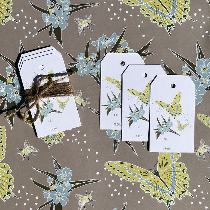 gift tag 3 pack with butterfly, bee, floral design, shown tied with twine laying on coordinating wrapping paper