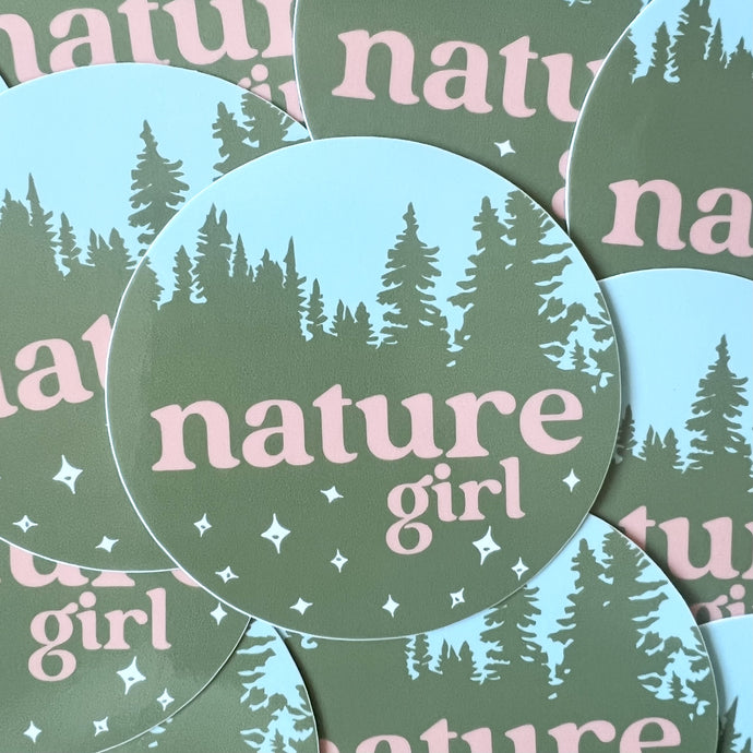 pile of circular stickers with an illustration of green pine trees and a blue sky, pink text reads nature girl