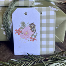 Load image into Gallery viewer, Closeup shot of a gift wrapped package and two TO/FROM gift tags with a floral and pinecone illustration on the front and a green gingham plaid print on the back..
