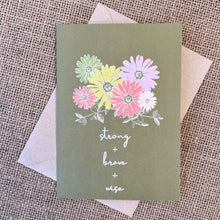 Load image into Gallery viewer, Greeting card with olive green background and colorful daisy flowers, text reading &quot;strong + brave + wise&quot;, styled with a kraft envelope on a tan burlap background
