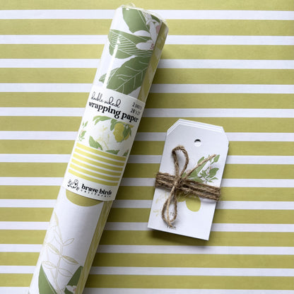 Packaged roll of wrapping paper  sitting on a flat sheet of the paper showing the full pattern, shown with coordinating gift tags
